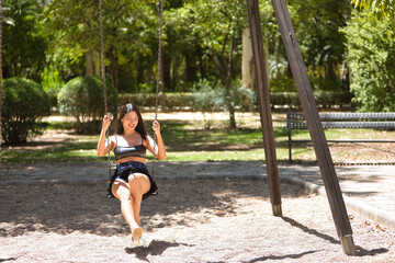 South American woman, young, pretty, brunette with leather top and short jeans, swinging on a swing very happy and smiling. Concept beauty, diversity, happiness, parks, games.