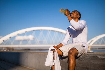 Portrait of young african-american man who is drinking refreshment drink and relaxing after jogging.
