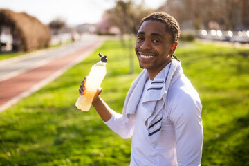 Portrait of young african-american man who is drinking refreshment drink and relaxing after jogging.