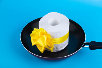 a roll of toilet paper wrapped in a gift bow lying in a frying pan. 