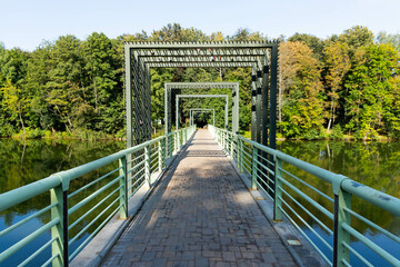 Pedestrian bridge over the river against the background of the river and trees and reflection in the water. - Powered by Adobe