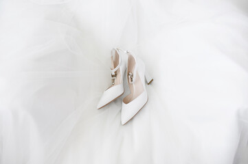 Layout: of white wedding shoes lie on a white wedding dress. Concept of wedding day, style, image, fashion. Top view.Morning preparations for the bride
