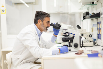 Male scientist analyzing specimen with microscope in a laboratory