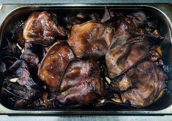 Close-up view of smoked pig ears in a metal tray, highlighting the texture and rich color from the smoking process