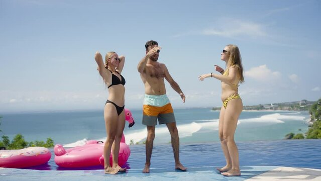 Group friends dance on infinity pool party in beach club with ocean view. Young people have fun together on summer vacation trip, celebrate holiday enjoy