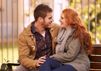 Couple, smile and sit on bench at park with affection in cold weather or winter, together and...