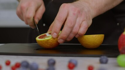 A close-up of a bright orange. In slow motion video of water droplets. The cook cuts the orange and we see the red juicy pulp. A kitchen knife cuts a juicy orange, drops of juice flow down. - Powered by Adobe