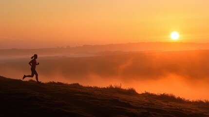 Fototapeta na wymiar Silhouette of a runner on a misty hillside at sunrise with a warm orange sky