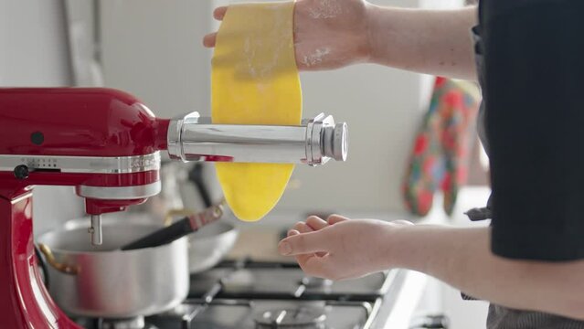 A person is using a red kitchen machine to roll out fresh, homemade pasta dough. The process highlights a home cooking experience, focusing on the creation of Italian cuisine with a domestic touch.