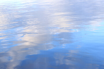 Reflection of clouds in water. The surface of water in a lake, river or flooded quarry. Ripples on the water. Beautiful color of water. Natural background