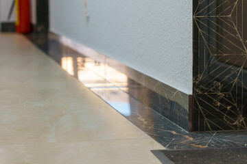 The detail of the corner baseboard on the wall and granite tiles on the floor. A white wall with a...