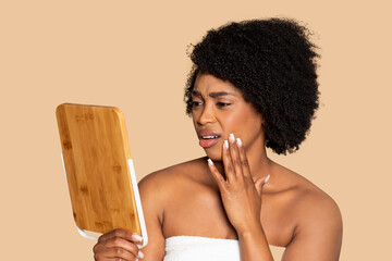 Worried black woman examining face in mirror, skincare focus