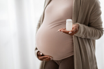 Unrecognizable pregnant young black woman holding jar with pills