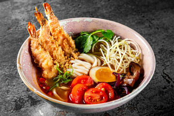 A vibrant bowl of ramen with crispy tempura shrimp, fresh vegetables, noodles, and a halved boiled...