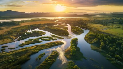 Aerial view of a meandering river at sunset with golden light reflecting on water, surrounded by lush greenery and distant mountains.