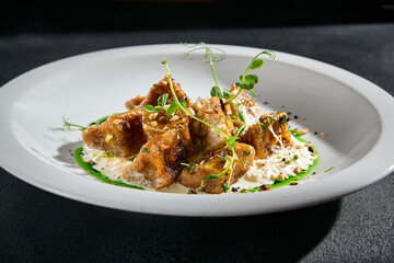 Crispy eggplant with stracciatella cheese and a drizzle of green sauce on a white plate, a closeup of a culinary delight