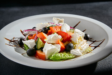 Greek salad closeup with feta cheese, Kalamata olives, and balsamic glaze on a white plate