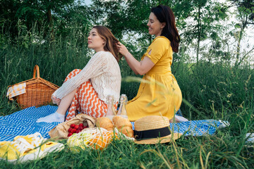 A young woman braids her friend's hair at a picnic in the park.