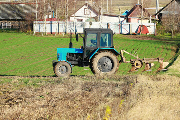 a blue tractor is plowing a field with a fence in the background.