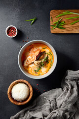 Top view of Tom Yum soup with seafood, herbs, and spices alongside a bowl of rice