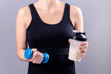 woman holds a glass of collagen in one hand and a dumbbell in the other.