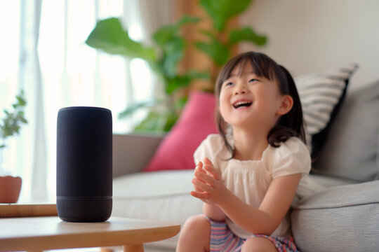 Laughing Asian girl interacting with smart speaker. Concept of the image suitable for advertising technology, smart home devices, and interactive educational tools for children