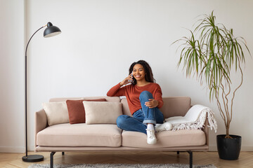 Relaxed young black woman enjoying conversation on her mobile phone at home