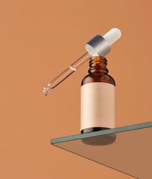 dropper bottle with clear liquid is placed on a glass shelf. The orange background contrasts with the bottle and dropper. A drop of liquid is visible at the tip of the dropper
