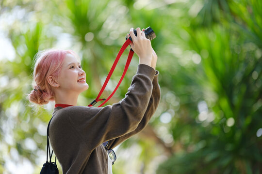 Beautiful Young artist Woman taking photo in flowers garden. Young cute girl carry the camera in the garden.