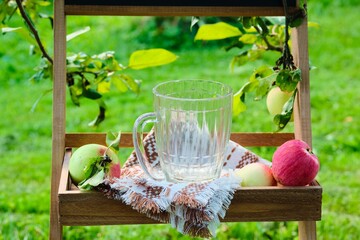 Empty glass mug for soft drinks on a wooden stand under fruit trees - obrazy, fototapety, plakaty