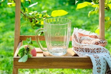 Empty glass mug for soft drinks on a wooden stand under fruit trees