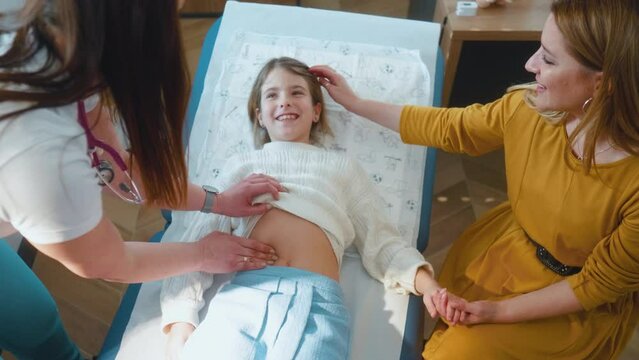 A female doctor examines the patient's stomach, conducting a clinical examination of the body little girl