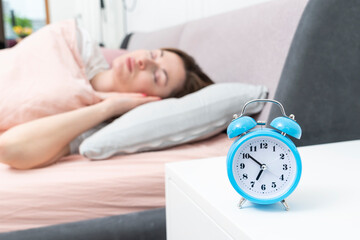Close up photo of alarm clock standing on nightstand and sleeping beautiful woman on the background in the bedroom