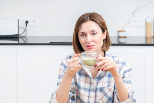 Close-up portrait of attractive girl drinking hot matcha tea in the kitchen	
