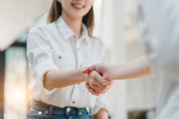 Close-up of a warm, friendly handshake between two professionals in a bright, casual setting, signaling a positive agreement.