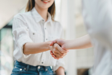 Close-up of a warm, friendly handshake between two professionals in a bright, casual setting, signaling a positive agreement.