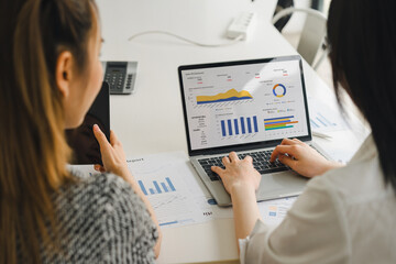 Two businesspeople or an accountant team are analyzing data charts, graphs, and a dashboard on a laptop screen in order to prepare a statistical report and discuss financial data in an office.