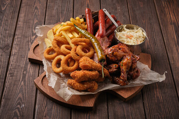hearty assortment of appetizers, including crispy onion rings, golden fries, grilled sausages, glazed chicken wings, and creamy coleslaw, is beautifully presented on a rustic wooden board - 763119179