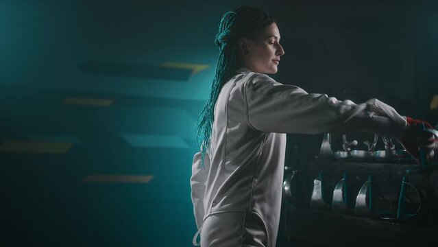 Side footage of Caucasian swordswoman suiting up and taking her rapier while preparin for fencing training in dark foggy hall