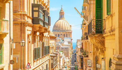 Sunny street in Valletta old town, St Paul’s Anglican Pro-Cathedral on a background - obrazy, fototapety, plakaty