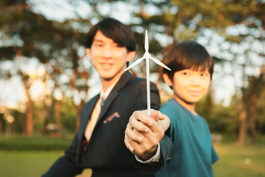 Asian boy and businessman holding wind turbine model together as Earth day concept as corporate social responsible to make greener with eco alternative energy for sustainable future generation. Gyre