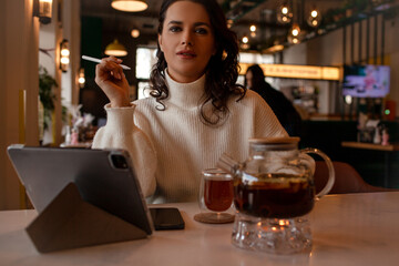 The girl works at the computer and drinks tea in cafe.