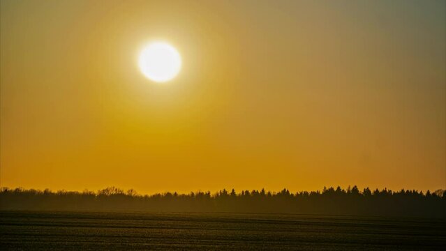 As time passes, the bright orange sun sets behind the clouds. Farmland timelapse