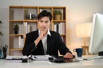 Confident millennial businessman sitting at workplace and looking at camera