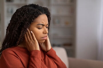 Fototapeta na wymiar Stressed young black woman holding her ears, suffering acute pain at home