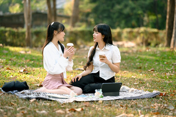 Carefree Asian women friends talking and enjoying coffee in the park after work