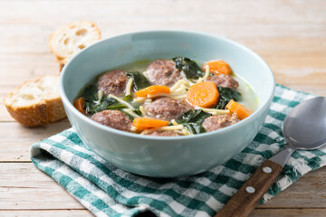 Italian Wedding Soup with meatballs and spinach on wooden table
