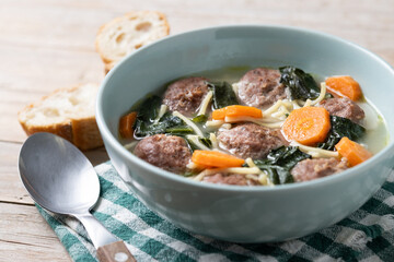 Italian Wedding Soup with meatballs and spinach on wooden table