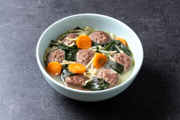 Italian Wedding Soup with meatballs and spinach on black slate background