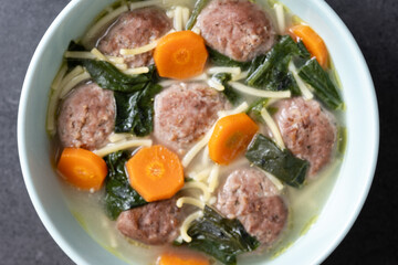 Italian Wedding Soup with meatballs and spinach on black stone. Close up